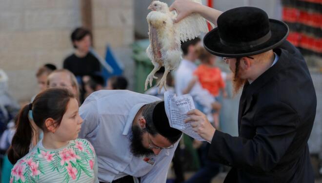 An ultra-Orthodox Jew swings a chicken over the head of a member of their family as they perform the Kapparot ceremony in an ultra-Orthodox neighbourhood in Jerusalem, on September 14, 2021. - Kapparot is a custom practised by some Jews, in which the sins of a person are symbolically transferred to a fowl, and is performed before Yom Kippur (Day of Atonement), the most important day in the Jewish calendar, which will start this year at sunset on September 15. (Photo by AHMAD GHARABLI / AFP) (Photo by AHMAD GHARABLI/AFP via Getty Images)