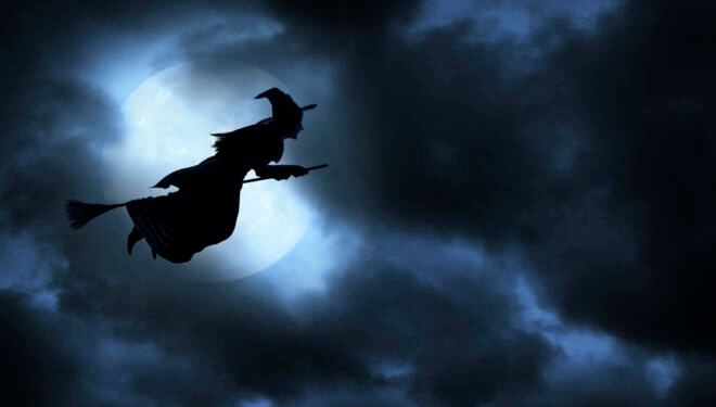 Witch flying on broom silhouetted against the moon.