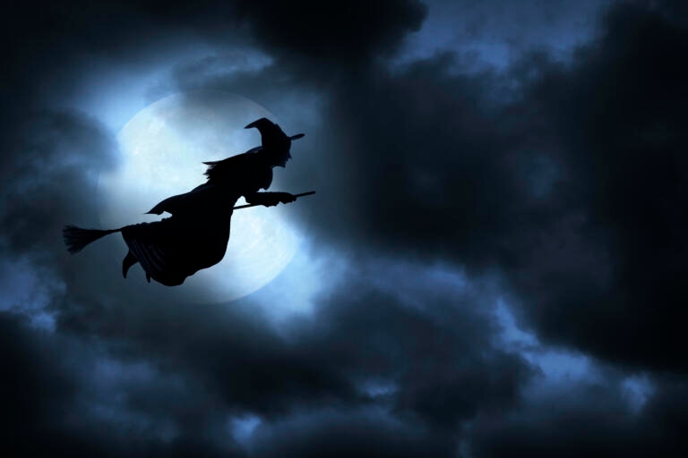 Witch flying on broom silhouetted against the moon.