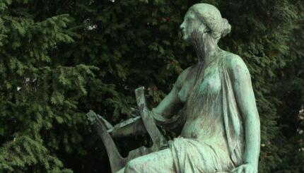 Weathered green statue of a woman playing a lyre.