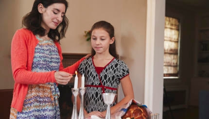 Jewish mother and daughter lighting candles for Shabbat meal