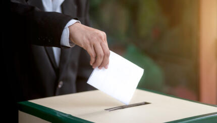 Hand of a person casting a vote into the ballot box during elections