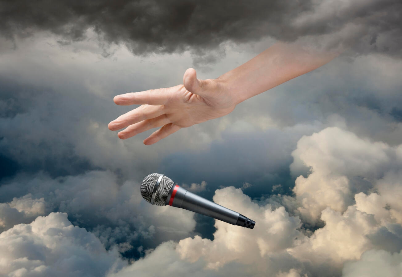 Caucasian hand dropping microphone in clouds