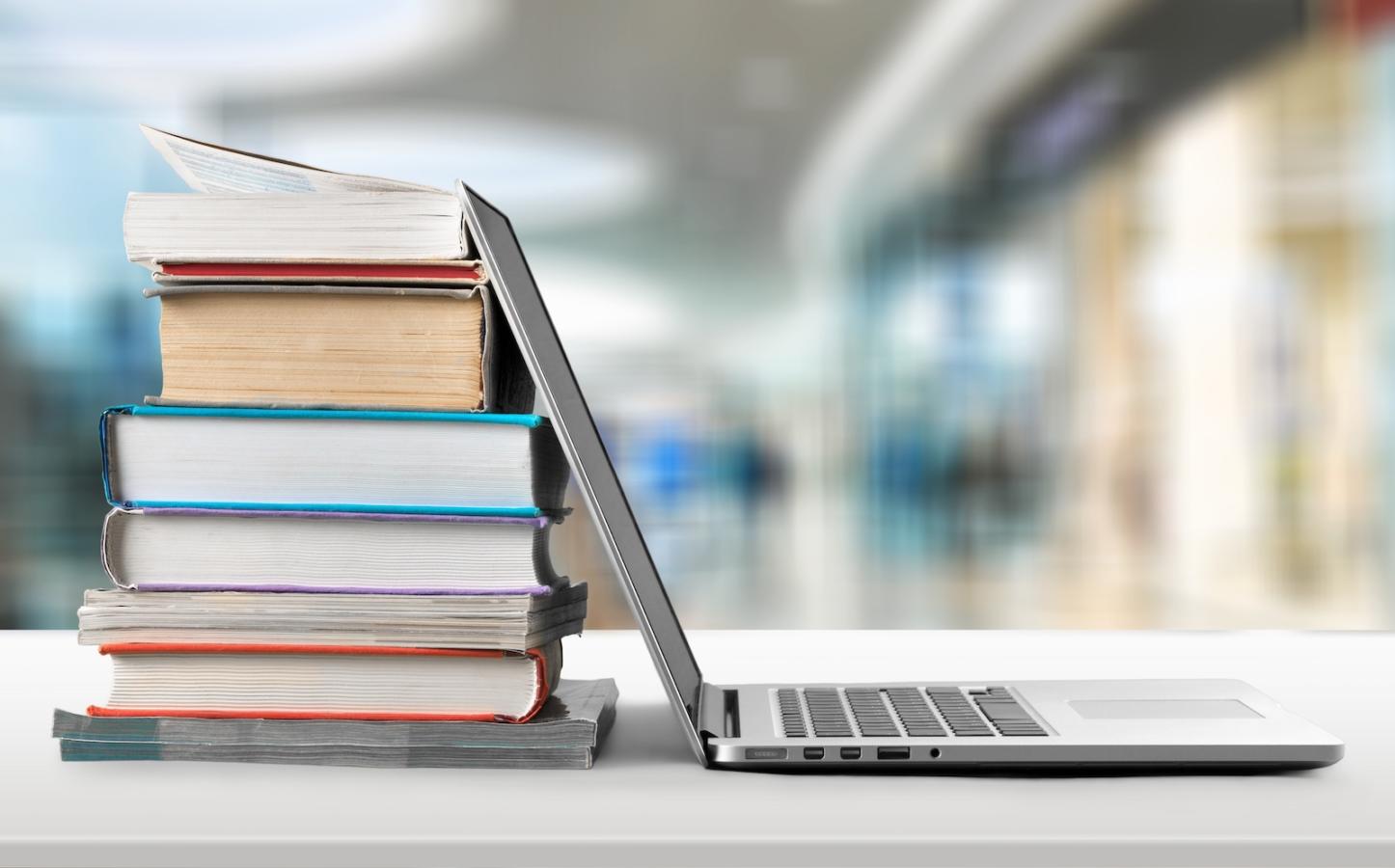 Stack of books with laptop on wooden table