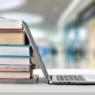 Stack of books with laptop on wooden table