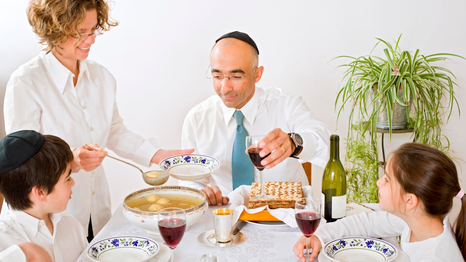 a Passover seder, including men wearing kippot or yarmulkes, and a table with matzo ball soup, wine, matzah and other traditional Passover foods