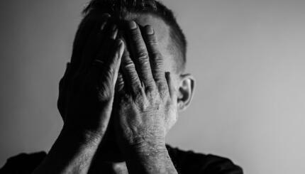 Black and white photo of a person clasping hands over their face.