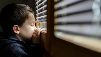 Small sad boy looking through the window during Coronavirus isolation.