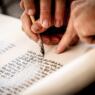 close up of hands scribing a torah scroll