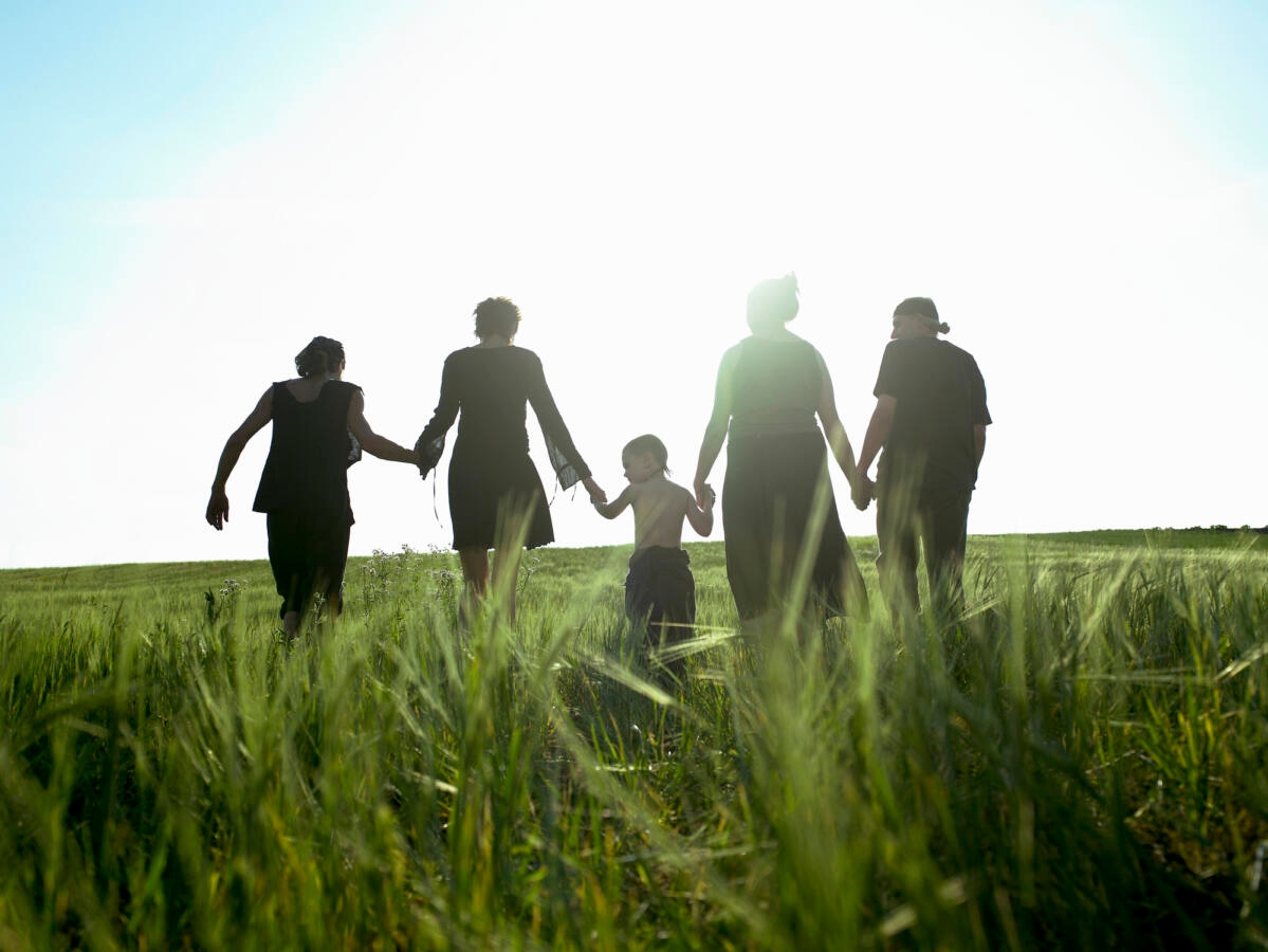 Sillhouette of people in a field holding hands.