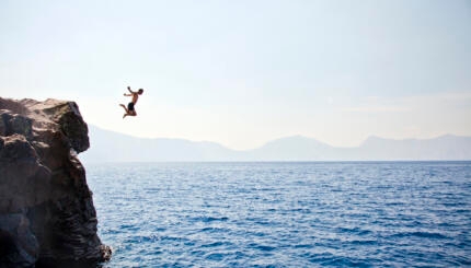 Young man jumping off of cliff into Crater Lake on sunny day, Crater Lake National Park, Oregon, USA