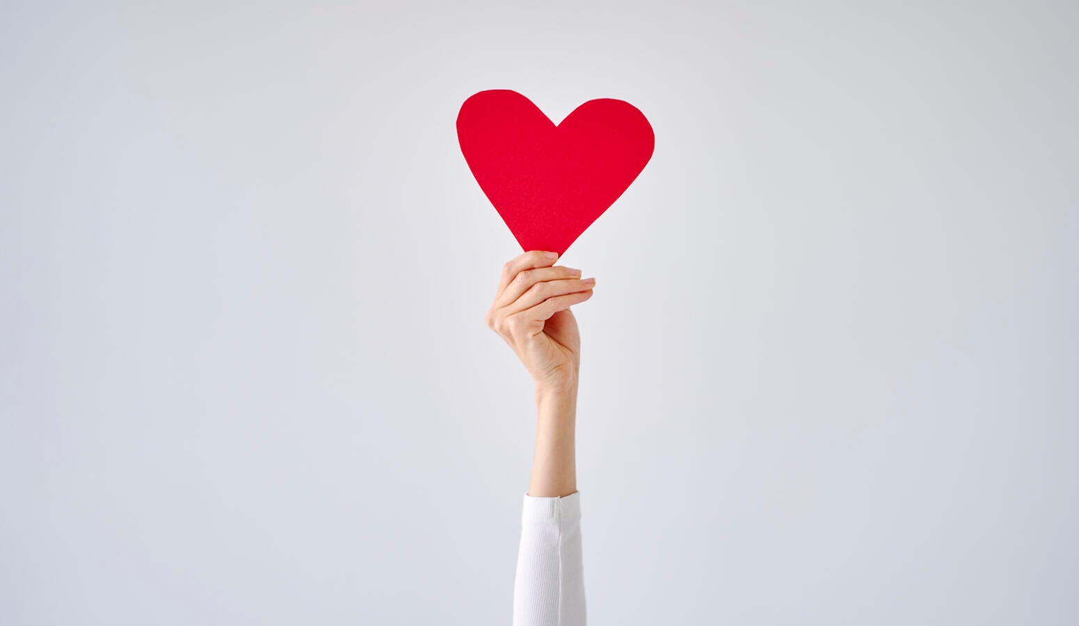 Female's hand holding red heart against white grey background.