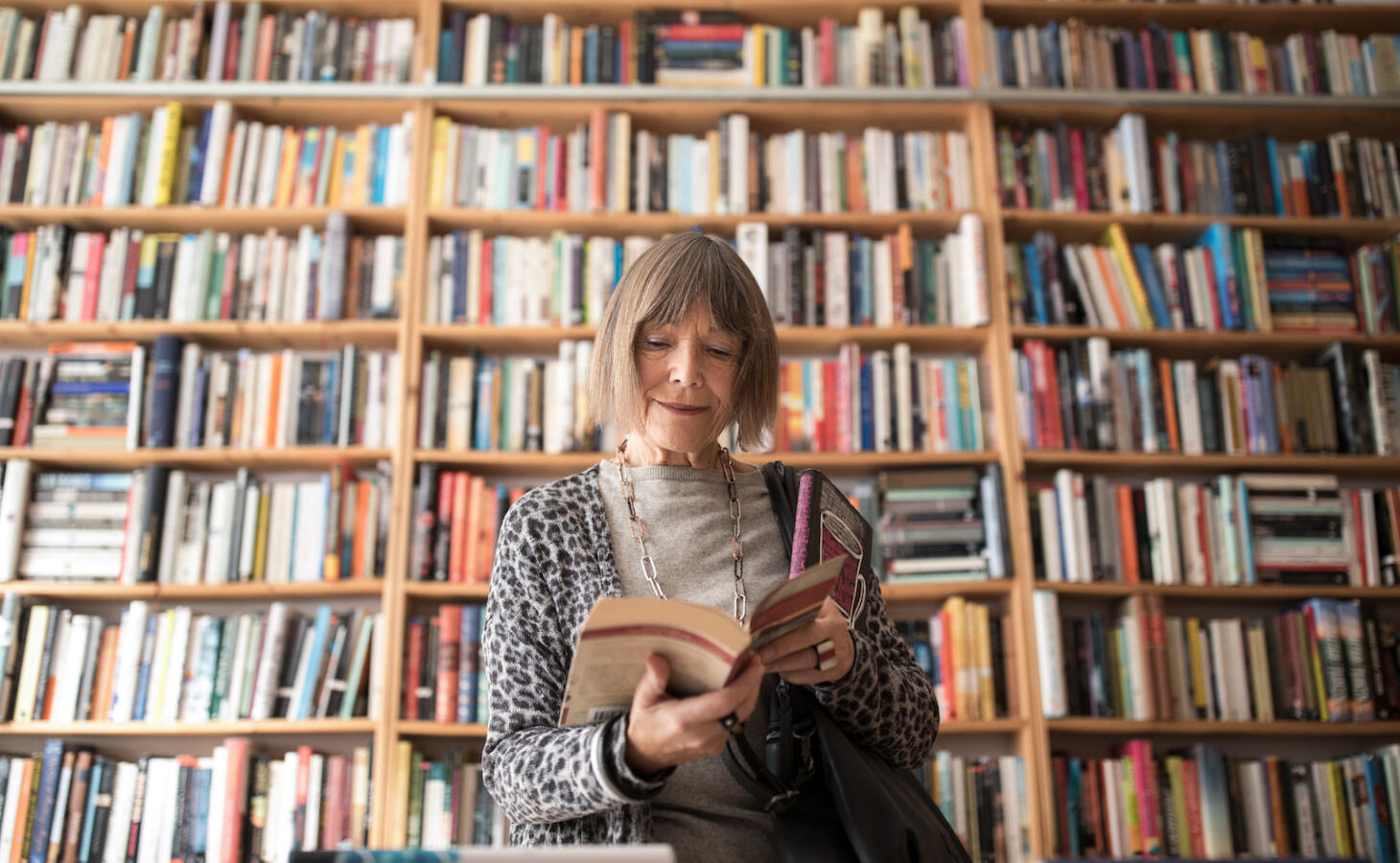 Senior woman reading book while standing against bookshelf at bookstore