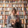 Senior woman reading book while standing against bookshelf at bookstore