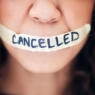 Closeup shot of an unrecognisable woman with tape on her mouth that has the word "cancelled" written on it