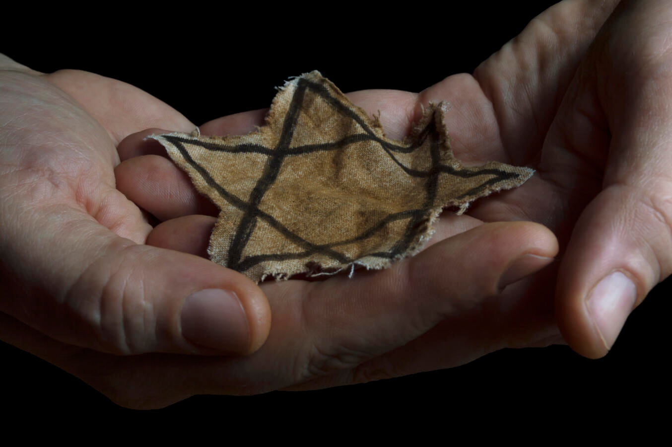 A faded Jewish star badge resting in someone's hands.