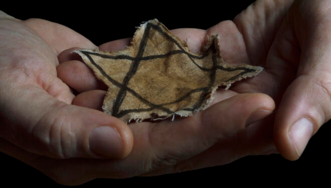 A faded Jewish star badge resting in someone's hands.