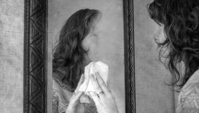 A woman uses a paper towel to wipe away her reflection in a mirror.