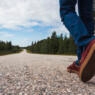 Finland, Lapland, feet of man walking on empty country road