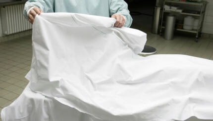 Photo of a doctor removing a sheet from a body